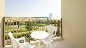 A balcony with a white table and chairs, a metal railing, and a view of a landscaped garden.