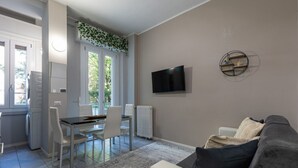 Un soggiorno moderno con un divano grigio, un'area pranzo con tavolo e sedie, una TV a parete e una finestra vista verde.