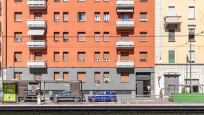 Un edificio a più piani con balconi, un'auto parcheggiata e un binario ferroviario in primo piano.