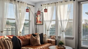 A living room with a brown leather sofa, white curtains, and a painting on the wall. - Rhythm Room | Oak Lawn 2BR Near Uptown, Pool & Gym (Dallas)
