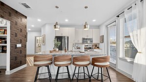 A modern kitchen with a central island, bar stools, and a dining area. - Rhythm Room | Oak Lawn 2BR Near Uptown, Pool & Gym (Dallas)