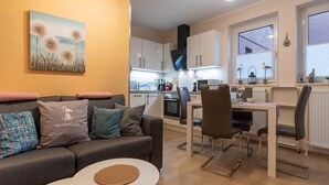 A modern living room with a grey sofa, a small white table, and a painting on the wall. - Ferienwohnung in Busum (Büsum)