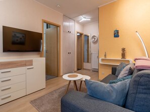 A modern living room with a sofa, a TV mounted on the wall, a small round table, and a wooden wardrobe. - Ferienwohnung in Busum (Büsum)