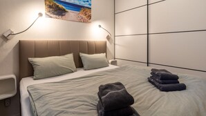 A hotel room with a bed, a painting of a beach scene, a wall-mounted light, and a bedside table. - Ferienwohnung in Busum (Büsum)
