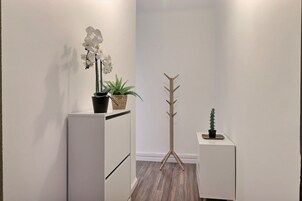 Un pasillo con paredes blancas, suelo de madera, un perchero y plantas en macetas.