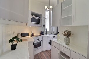 Una cocina compacta con muebles blancos, un microondas, un tostador y un lavamanos.