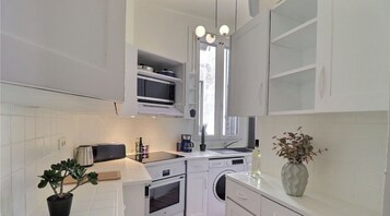 Una cocina moderna con armarios blancos, microondas integrado, cafetera y lavadora.