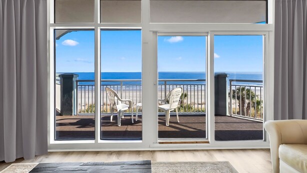 Ein Zimmer mit einer großen Schiebeglastür, die auf einen Balkon mit zwei weißen Stühlen und Meerblick führt.