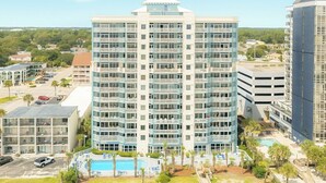 Ein mehrstöckiges Hotel mit Innenhof, der einen Swimmingpool, Palmen und einen Parkplatz umfasst.