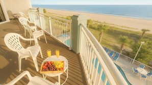 Ein Balkon mit weißen Plastikstühlen, einem Tisch mit einer Fruchtplatte und zwei Gläsern Orangensaft, mit Blick auf den Strand.