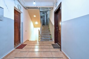 Un couloir avec une porte en bois sur la gauche, un escalier en bois au centre et une porte en bois sombre sur la droite.