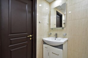 Une salle de bain avec une porte en bois foncé, un lavabo blanc et un miroir au-dessus.