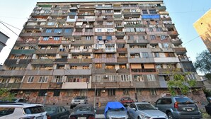 Un edificio residenziale a più piani con balconi, condizionatori e un'area di parcheggio antistante.