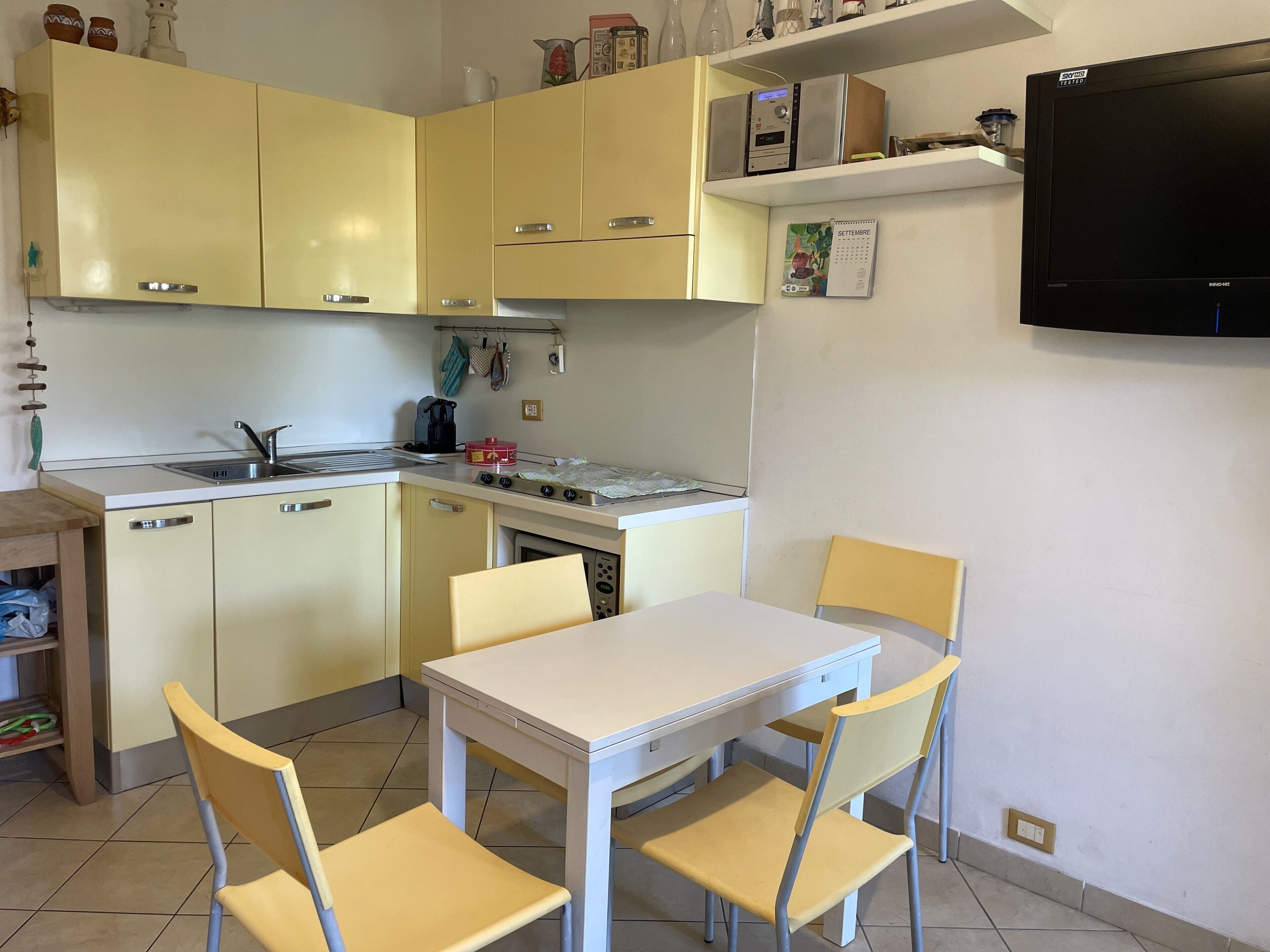 Cozinha compacta com área de refeições, incluindo pia, fogão e uma TV de tela plana na parede.