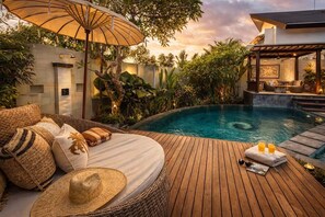 A wooden deck with a pool, a wicker sofa with cushions, a straw hat, and a table with drinks. - Villa St Calyx by DVH Luxe Retreats 3BR (Canggu)