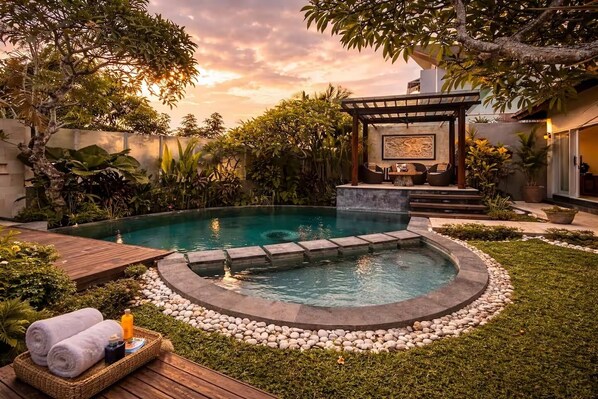 Une piscine dotée d’un jacuzzi circulaire, entourée d’une bordure en pierre, avec une terrasse en bois et des chaises longues.