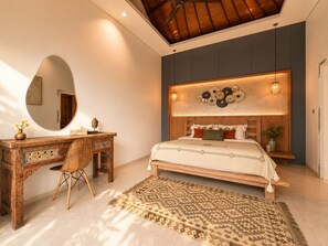 A bedroom with a wooden bed, a desk with a chair, a large mirror, and a decorative wall. - Villa St Calyx by DVH Luxe Retreats 3BR (Canggu)