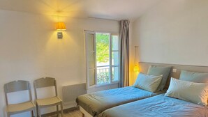 A bedroom with two beds, a chair, a small table, and a window with curtains. - La Maison de Vacances 3 minutes from the ocean (La Flotte)