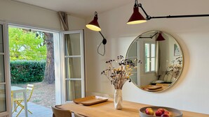 A dining area with a wooden table, chairs, a vase with dried flowers, a mirror, and a bowl of fruit. - La Maison de Vacances 3 minutes from the ocean (La Flotte)