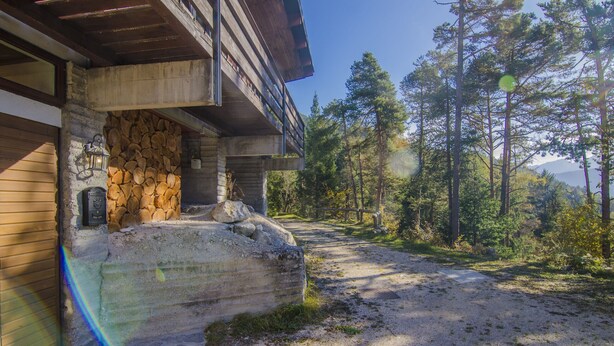 Un chalet rustique avec un mur en pierre et une terrasse en bois, entouré d ’une zone boisée.