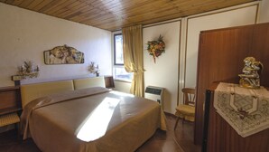 Une chambre avec un grand lit, une tête de lit en bois, une petite table ornée d’un objet décoratif, une chaise et une fenêtre avec des rideaux.