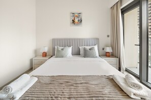 Habitación de hotel moderna con una cama grande, dos mesitas de noche con lámparas, vista a la ciudad a través de un ventanal grande y un cuadro en la pared.