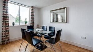 Un comedor con una mesa de vidrio y sillas negras, una ventana con cortinas estampadas y un espejo en la pared.