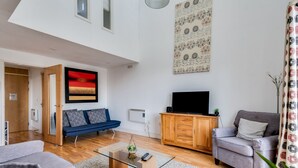 Una sala moderna con un sofá, un sillón y un televisor sobre un mueble de madera.