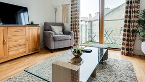 Una sala de estar moderna con una mesa de centro de vidrio, un sofá gris, armarios de madera y vista a un patio.