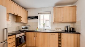 Een moderne keuken met houten kastjes, een zwart aanrecht, een magnetron, een waterkoker en een bord met koffie aanbiedingen.