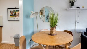 Een ronde houten tafel met vier stoelen, een spiegel, een lijst met foto en een klein plankje met een plant en een camera.