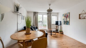 Een moderne woonkamer met een houten eettafel, stoelen, een bank, een televisie en een groot raam met gordijnen.