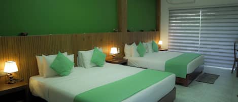 A hotel room with two beds, green bedding, wooden headboard, bedside lamps, and a large window with blinds.