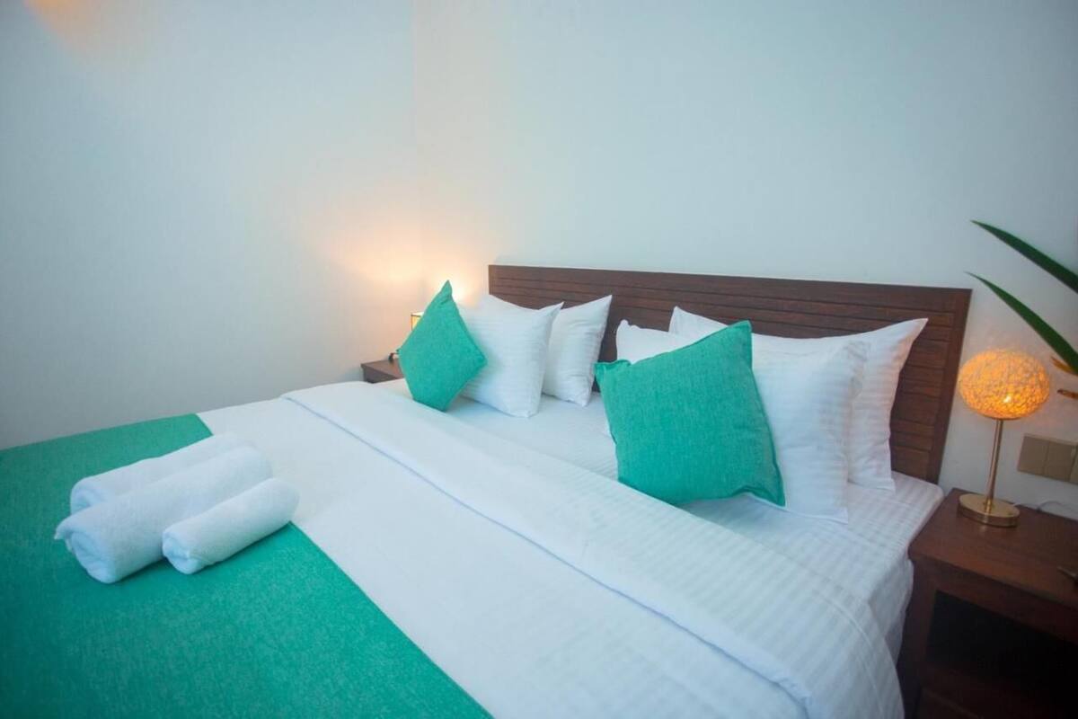 A neatly made bed with white and green bedding, a wooden headboard, and a bedside lamp.