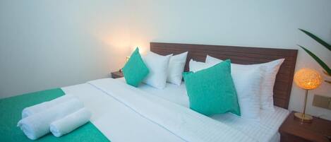 A neatly made bed with white and green bedding, a wooden headboard, and a bedside lamp.