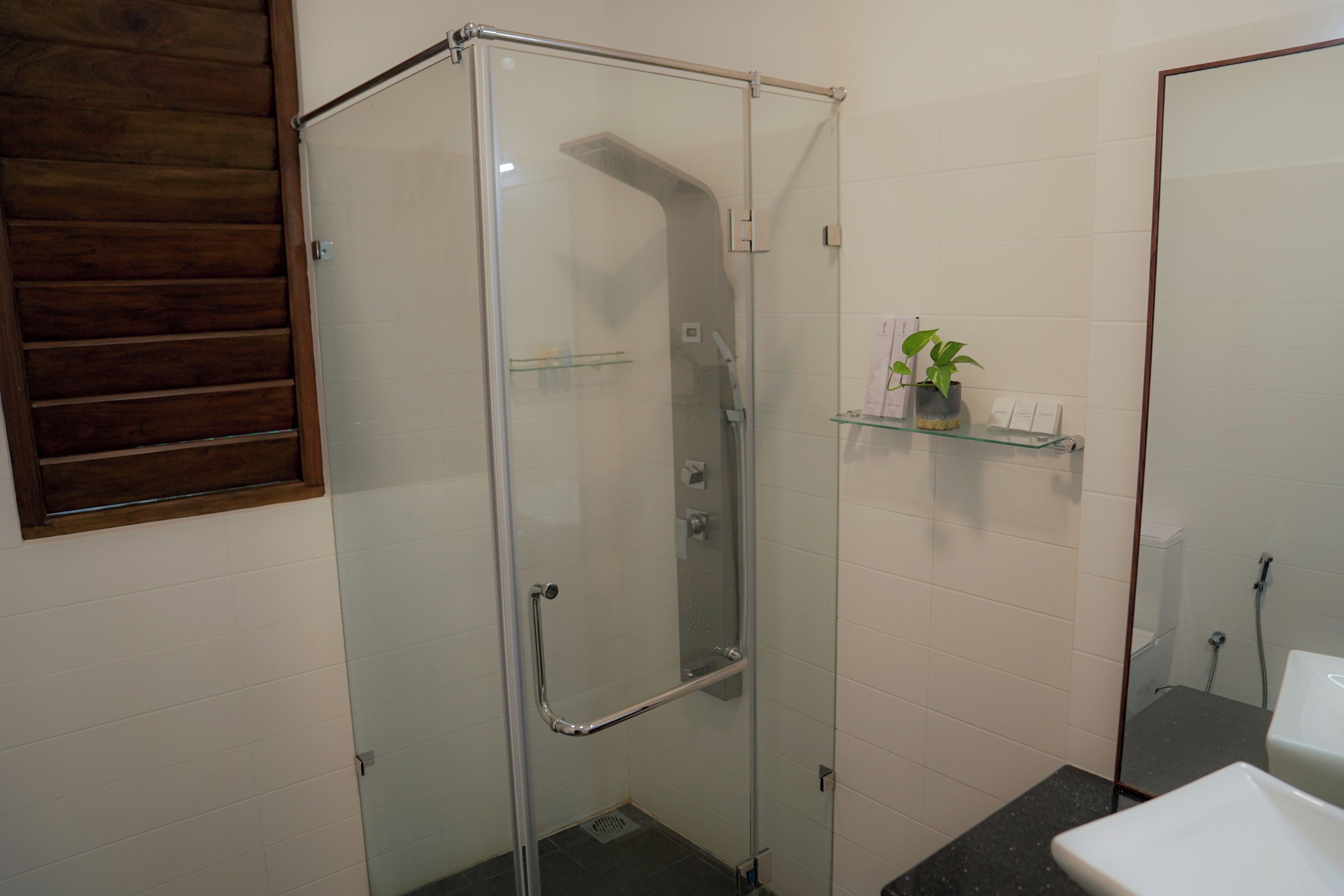 A glass-enclosed shower with a glass shelf holding toiletries.