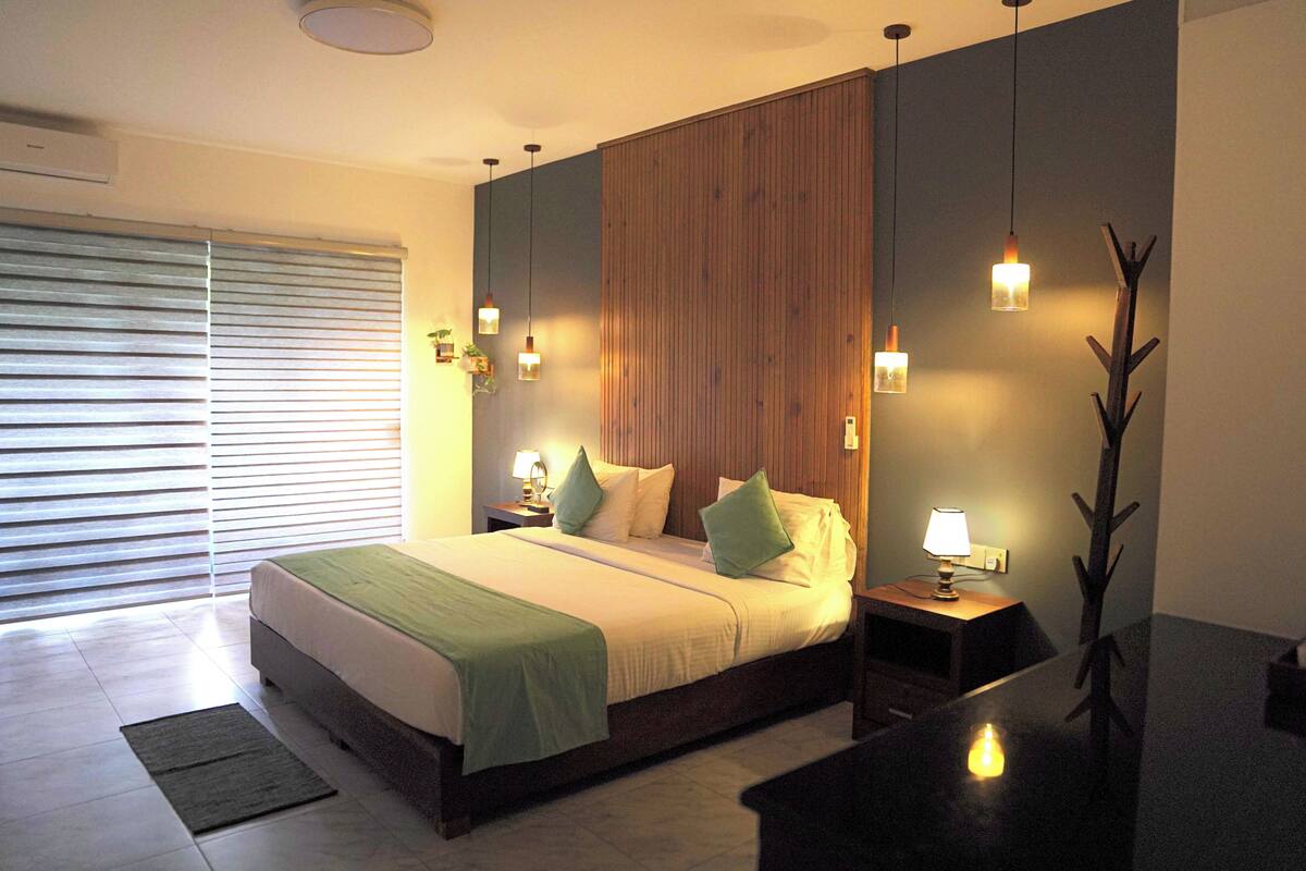 A modern bedroom with a large bed, bedside tables with lamps, a wooden accent wall, and a view of a balcony.