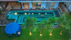 An aerial view of a swimming pool area with a person swimming, surrounded by greenery and potted plants.