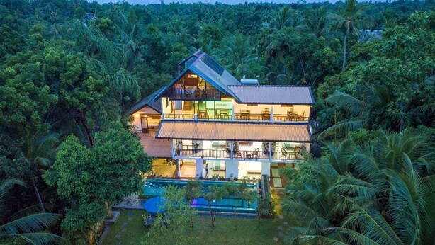 A two-story building surrounded by dense tropical vegetation, featuring a swimming pool and multiple balconies.