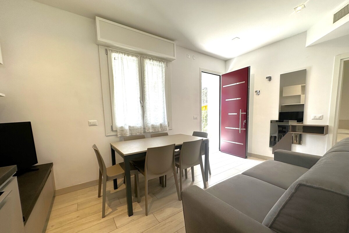 Un salon moderne avec un canapé gris, une table à manger avec des chaises, un téléviseur et une porte rouge.