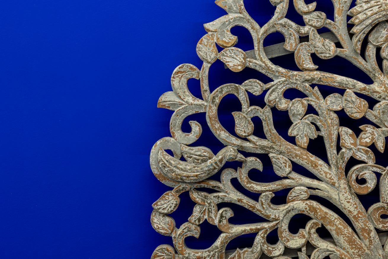 A close-up of a decorative metal piece with intricate designs against a blue background.