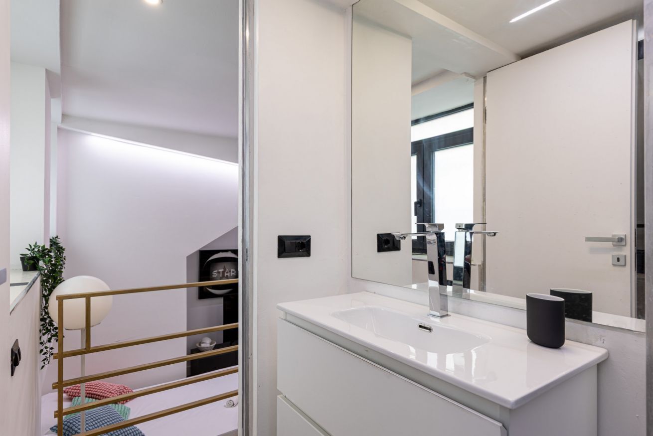 A modern bathroom with a large mirror, white sink, and a glass partition.