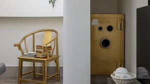 Ett rum med en trästol, böcker, en vit vägg, en trädörr med ett runt fönster och en tv som står på ett stativ.