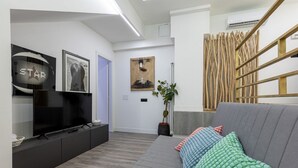 Ett modernt vardagsrum med en grå soffa, en platt-TV och en prydnadsväxt.