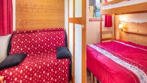 Una habitación con una cama litera y un sofá cama, ambos con ropa de cama roja.