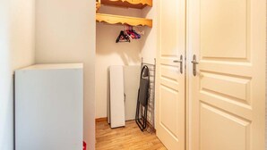 Un pasillo estrecho con una puerta blanca a la derecha y un refrigerador blanco a la izquierda, además de un tendedero con ropa colgando.