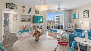 Sala de estar com vista para a cidade, área de jantar com mesa de vidro e sofá azul.