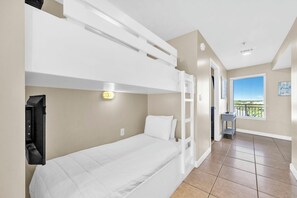 A hotel room with a bunk bed, a desk, a chair, a window with a view, and a small balcony.