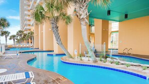 Área de piscina com espreguiçadeiras, palmeiras e um edifício com varandas.