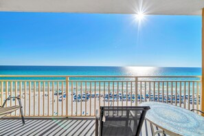 A balcony with a view of a beach, a table, and chairs.